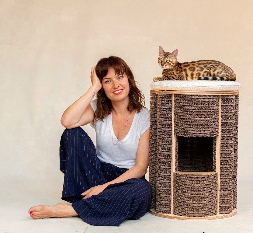 Woman dressed in blue shirt and pants sitting next to a cat and modern cat furniture