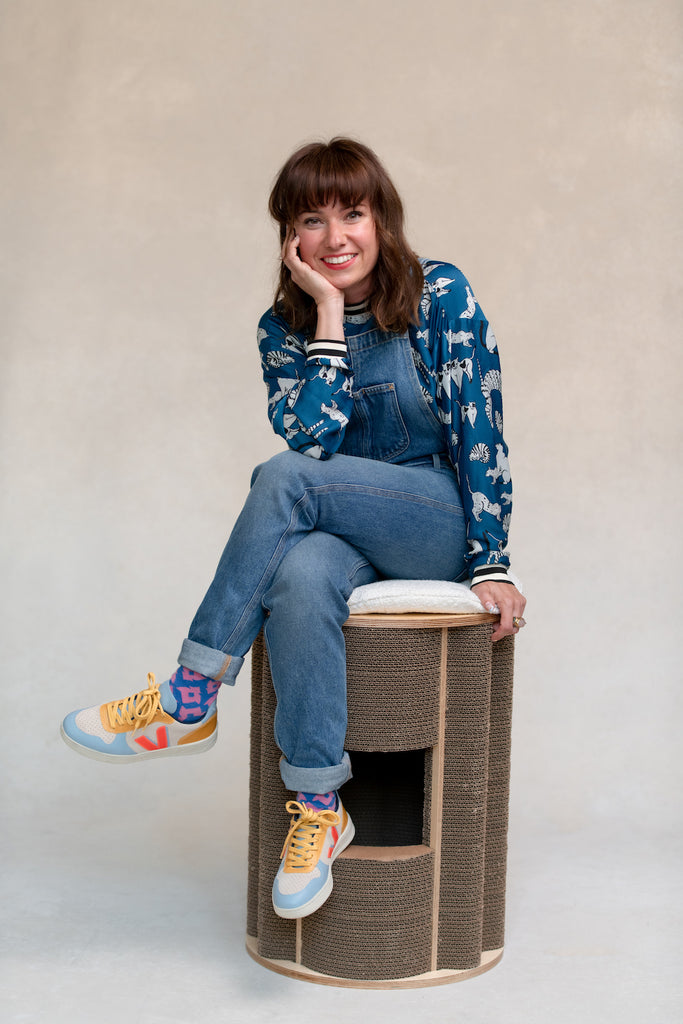 Woman dressed in jeans overalls and blue shirt sitting on cat modern furniture in brown and white